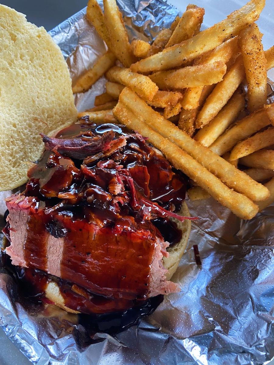 Smoked brisket sandwich with BBQ sauce and seasoned fries from Rolling Smokehouse BBQ trailer